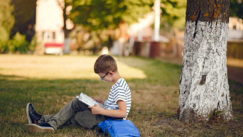 A child reading a book under a tree