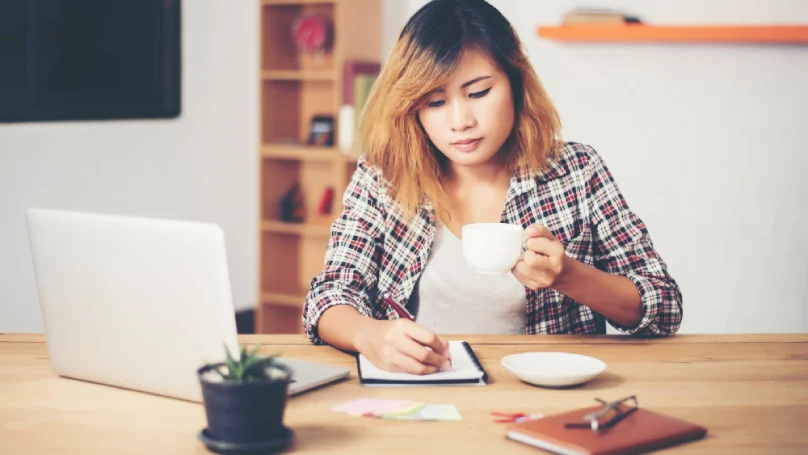 A student creating a schedule on a laptop with a cup of tea nearby